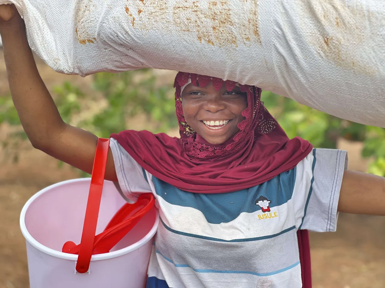 Mulher de uma comunidade carrega um balde e um saco com ajuda humanitária.