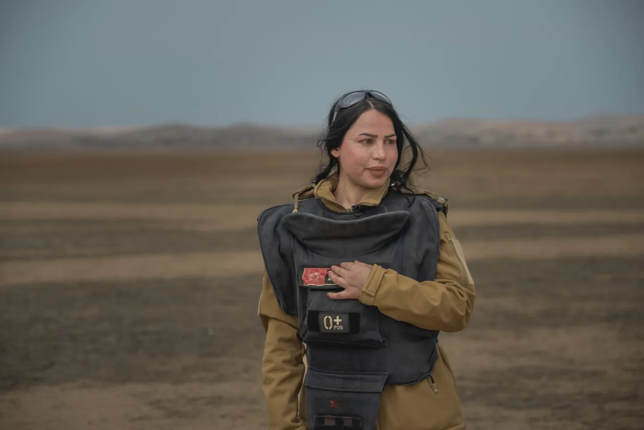 Noora Murad, a deminer wearing protective gear, looks at the camera from a mine field in Iraq.