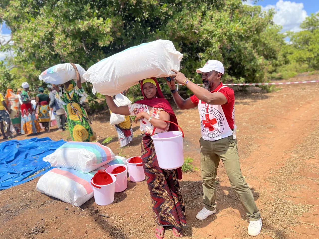 Colega do CICV ajuda uma mulher retornada durante uma distribuição em uma comunidade remota em Mueda. Credito: Fidelto Bata Colega do CICV ajuda uma mulher a carregar sacos de ajuda.