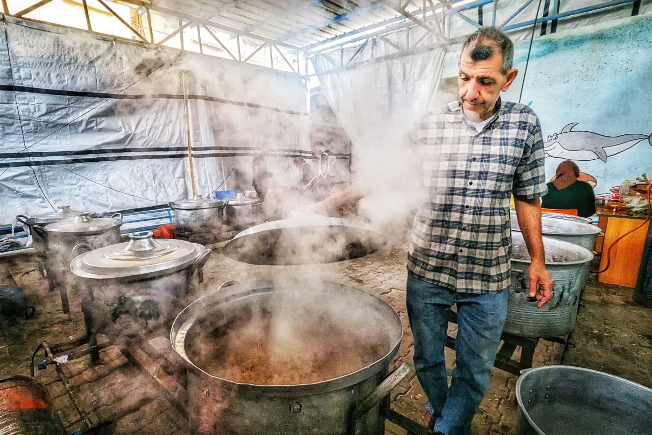 A man stirs a large vat of food in the community kitchen