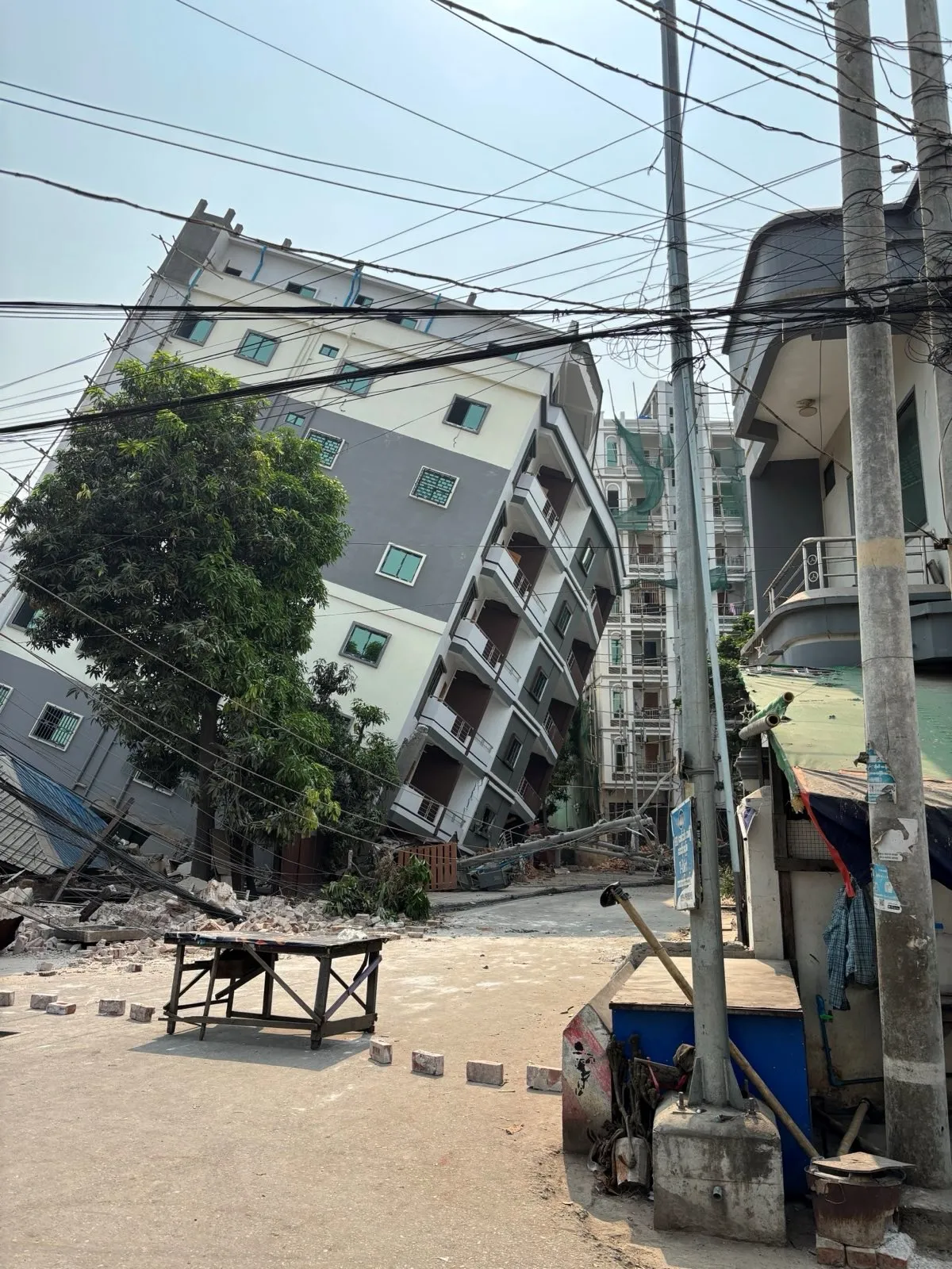 Un edificio de varios pisos se inclina peligrosamente tras un fuerte terremoto en Myanmar, con escombros e infraestructuras dañadas visibles en primer plano.