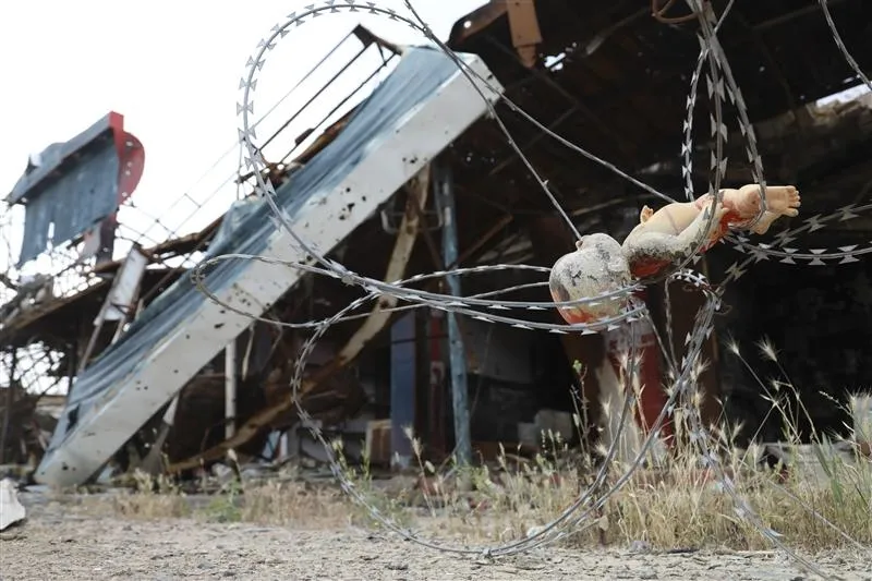 This doll, its head and face partly burned, is caught in barbed wire near an industrial facility. It may have been left behind by a fleeing child. Its position says much about the effects of war on children.