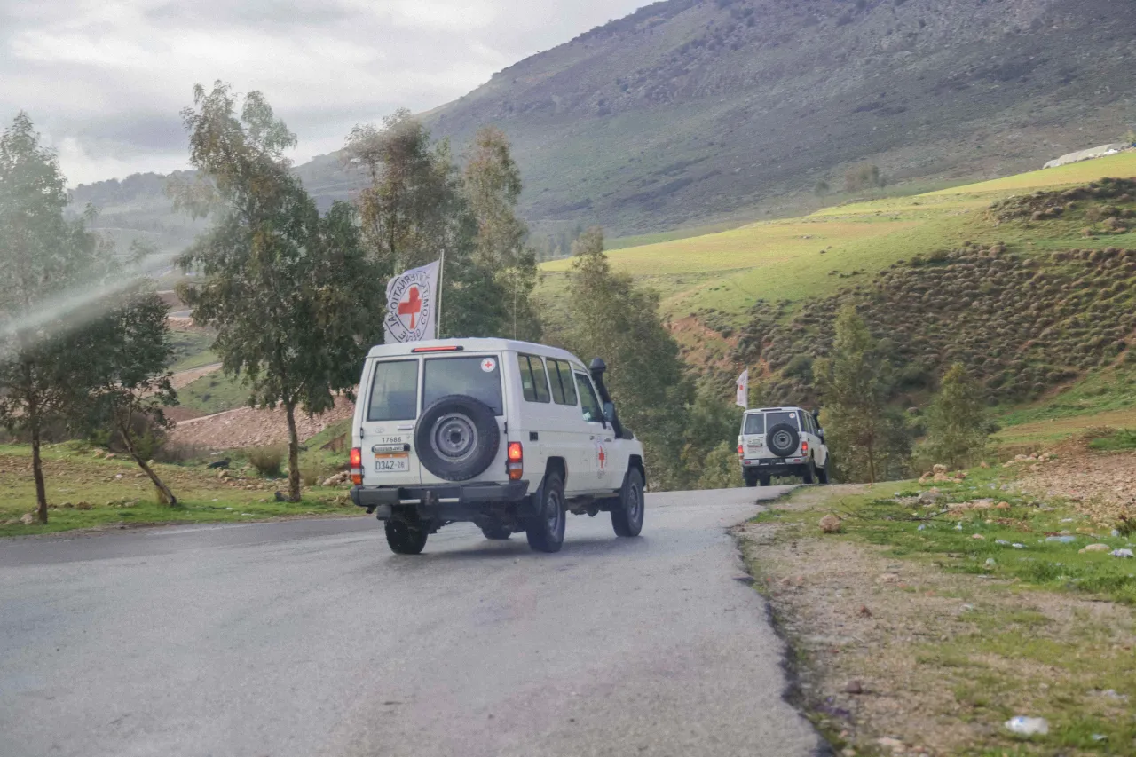 Two ICRC vehicles drive along a rural road in Lebanon, traveling through mountainous terrain to support water supply and other essential services for communities in need.