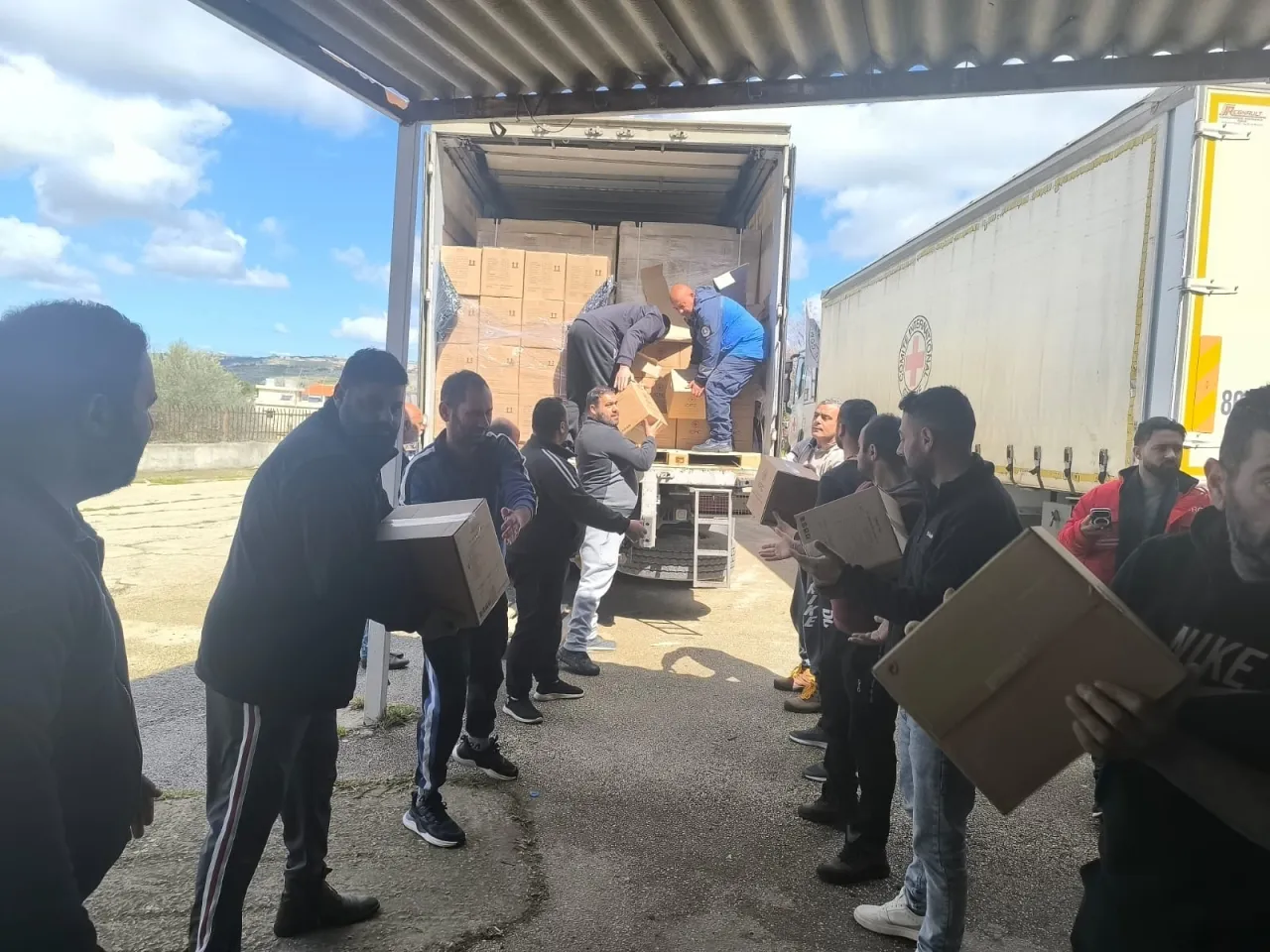 People forming a line to receive cardboard boxes being unloaded from the back of a truck.