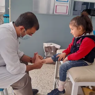 An ICRC doctor checking the ankle of a child seated on an examination table, in Afghanistan.