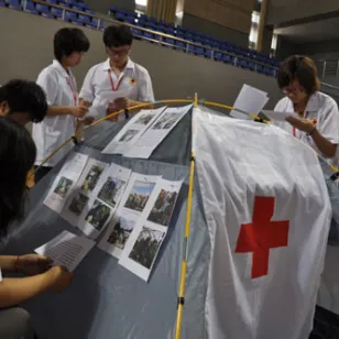 学生们围在挂满介绍文字和图片的简易帐篷旁，了解因武装冲突而流离失所、住在帐篷里的人的特殊处境。学生们还一起评估并计划分发哪些救援物资来满足人们的需要。