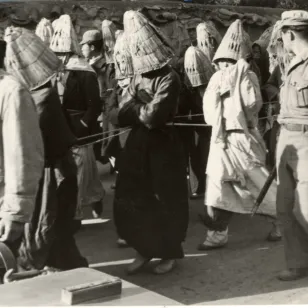 Detainees, tied to each other, with their heads covered by a straw hat to prevent identification (11 December 1950)