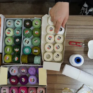 A hand reaching for a spool of thread amongst a colourful collection