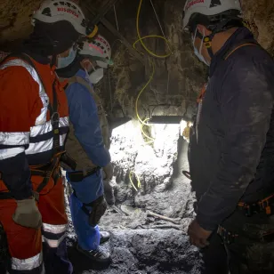 Especialistas de ciencias forenses e igeniería y un fiscal miran una fosa.