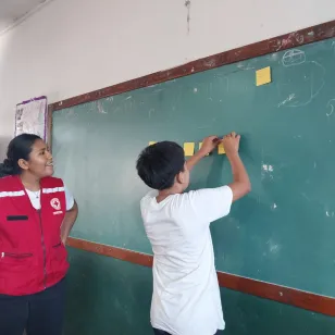 Una voluntaria en un ejercicio donde un niño anota algo en una pizarra.