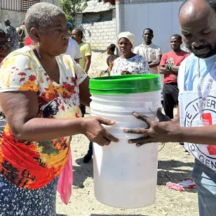 An ICRC staff helps a woman in Haiti to carry some buckets.