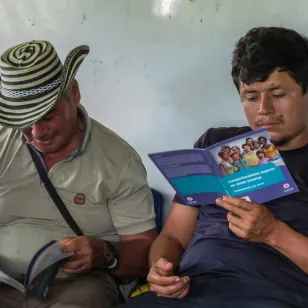 Dos personas de la comunidad leen con atención materiales del CICR, cada una sosteniéndolo en sus manos mientras se concentran en la lectura