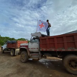 Una persona se encuentra sobre un camión, junto a una bandera del CICR, marcando la presencia humanitaria en el lugar.