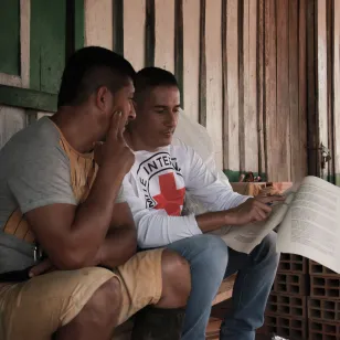 Una persona del CICR comparte un material con otra, mientras ambos lo observan con atención. Sentados en unos escalones, la imagen en plano diagonal capta su concentración en el documento.