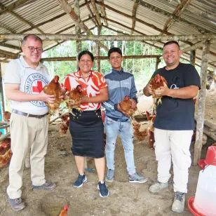 Personas de la comunidad y del CICR dentro de un gallinero sostienen gallinas y posan para la foto.