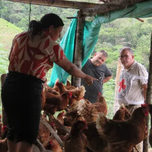 Una mujer dentro del gallinero señala algo, mientras una persona de la comunidad y un integrante del CICR la observan desde afuera.