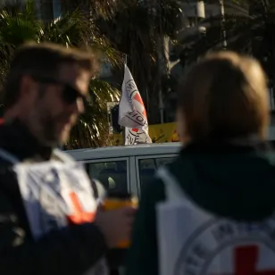 Two ICRC staff members wearing Red Cross vests speak beside an ICRC vehicle displaying a Red Cross flag in Lebanon during humanitarian operations amid escalating hostilities.