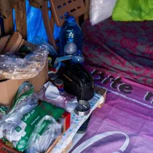 Personal belongings, including water containers, food items and bedding, are arranged inside a makeshift shelter