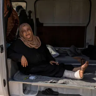 Saada sits at the open back of a van where she lives with her extended family, with bedding and personal belongings arranged inside 