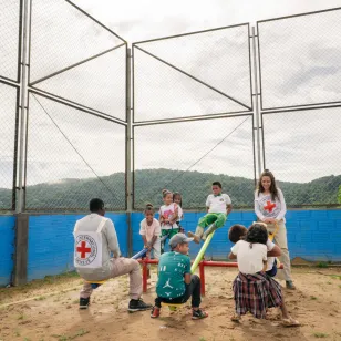 Niños y niñas juegan en un subibaja acompañados por personas del Comité Internacional de la Cruz Roja.