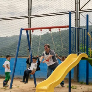 Niños y niñas juegan en los columpios acompañados por personas del Comité Internacional de la Cruz Roja.