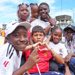 Un grupo de niños sonríe a la cámara mientras hacen un gesto de amor con las manos.