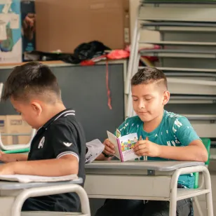 Un niño lee una cartilla dentro de un salón de clases.