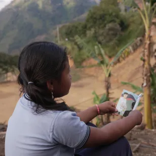 Una niña lee una cartilla en una montaña, mientras al fondo se aprecia un paisaje de Colombia.