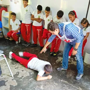 Un niño participa en un taller de comportamientos seguros mientras una persona del Comité Internacional de la Cruz Roja le indica por dónde desplazarse arrastrándose en el suelo.