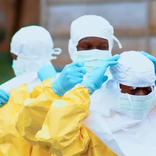 Red Cross volunteers help each other put on personal protective equipment before carrying out Ebola-related burial and response activities in the Democratic Republic of the Congo.