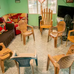 Sala de una vivienda con varias sillas dispuestas en círculo. Alrededor se observan sofás, un televisor, un ventilador y fotografías familiares.