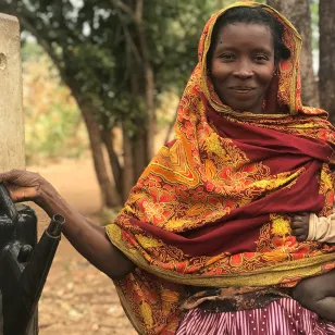 A woman carrying a child fills up a garden sprinkler in her other hand.