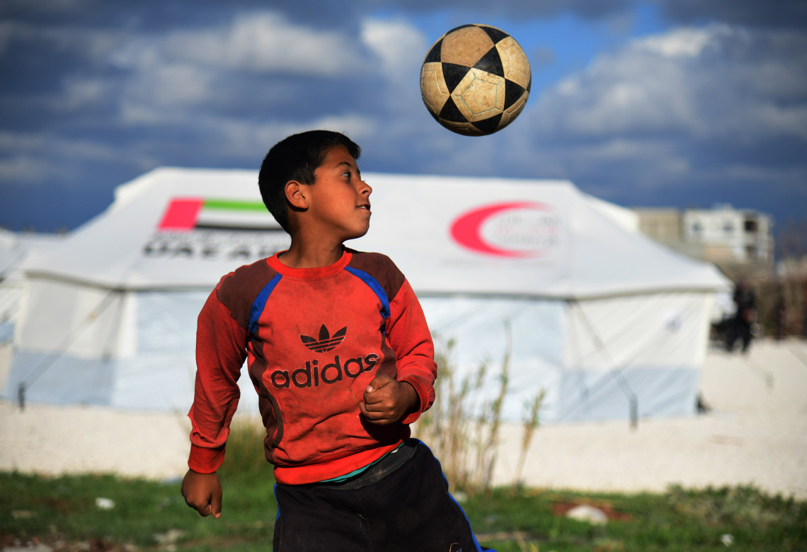 2023年3月9日，在叙利亚杰卜莱的一处灾民安置营，一个男孩在帐篷前踢足球。 