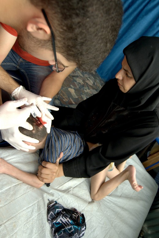 Quando os serviços de saúde colapsam, todos correm riscos. Neste posto de saúde do Crescente Vermelho Árabe Sírio, um médico examina uma criança ferida.