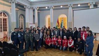 Policías, militares y otros funcionarios con miembros del Movimiento de la Cruz Roja posan para una foto grupal en un salón.