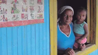Una mujer con su hijo en brazo miran por la ventana de su hogar en Colombia.