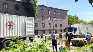ICRC trucks with a yellow car and people in the foreground