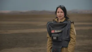 Noora Murad wearing protective gear looks at the camera from a mine field in Iraq.