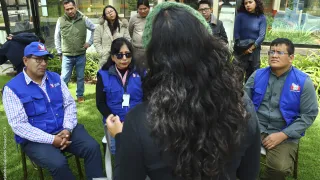 Trabajadores de la Defensoría del Pueblo observan a una mujer que aparece de espaldas en la foto.
