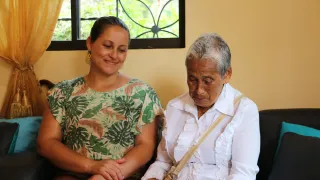 Una mujer mira una fotografía de una manera emotiva, mientras otra persona la acompaña, mientras sonrie y mira la foto también