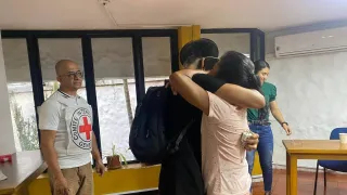 Dos personas se abrazan, mientras otras dos personas presencian el momento de reencuentro