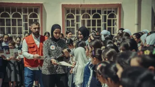 Two ICRC staff members interact with a group of primary school children. Some of the children are reading leaflets