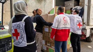 ICRC and Red Crescent staff unload boxes of humanitarian supplies from a truck, working together to deliver aid.