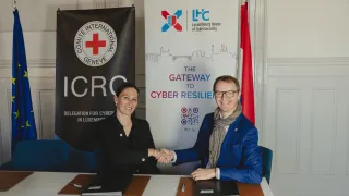 Head of ICRC Global Cyber Hub shaking hands with the CEO of Luxembourg House of Cybersecurity in front of the roll-ups of the respective organizations. With the flags of the European Union and Luxembourg next to the roll-ups.