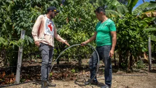 Un señor de la comunidad está junto a un trabajador del CICR. El señor está sosteniendo una mangera de donde sale agua