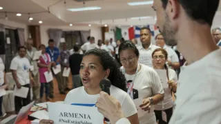 Mulher fala ao microfone segurando cartaz que diz: "Armênia. Não estão sozinhos"