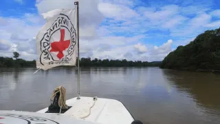 Bandera del CICR en una lancha junto a un paisaje ribereño.