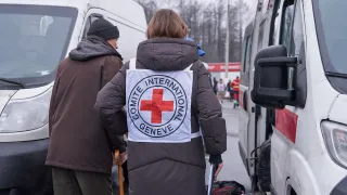 Сотрудница МККК сопровождает пожилого мужчину. 