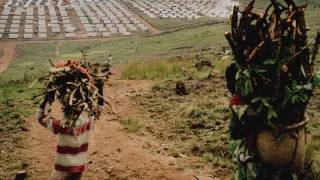 Personas refugiadas transportan suministros hacia el campamento de Busuma, hogar de comunidades congoleñas que han huido del conflicto. Al fondo se observan filas de refugios en el campamento. 4 de marzo de 2026, Busuma, Burundi.