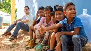Un grupo de niños y niñas están sentados junto a un trabajador del CICR. Están sonrriendo.